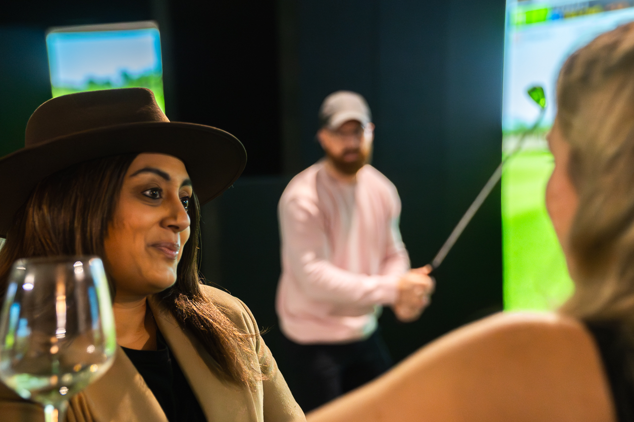 Indoor golf simulators at a networking event, blending business and leisure.