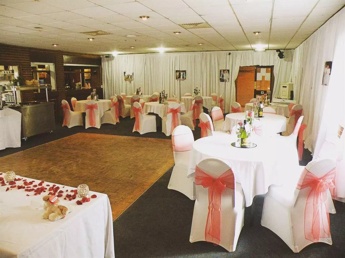 Elegant wedding event space at Staines Rugby Club with white linens and pink sashes.