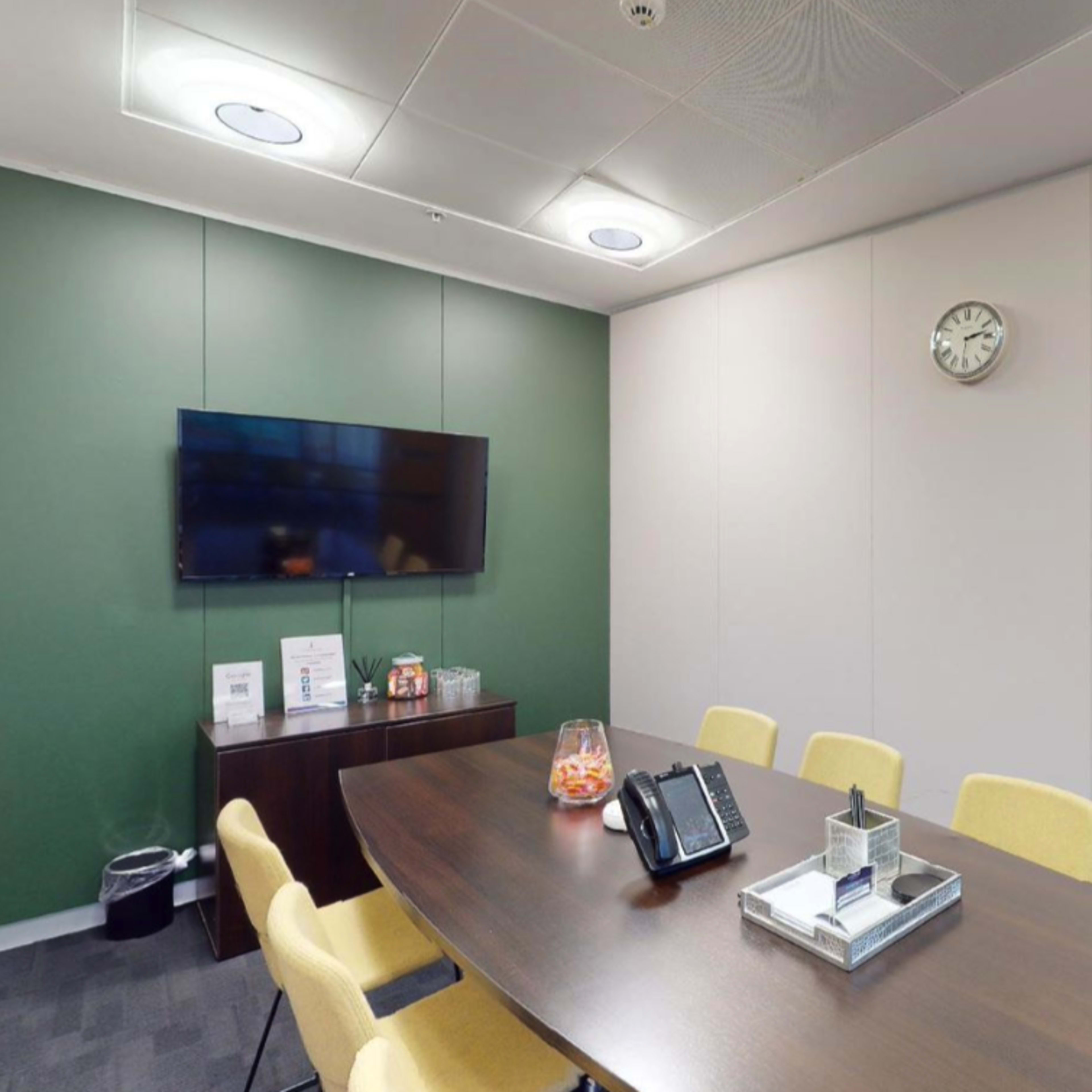 Modern meeting room for rent in Manchester with vibrant green wall and large screen.