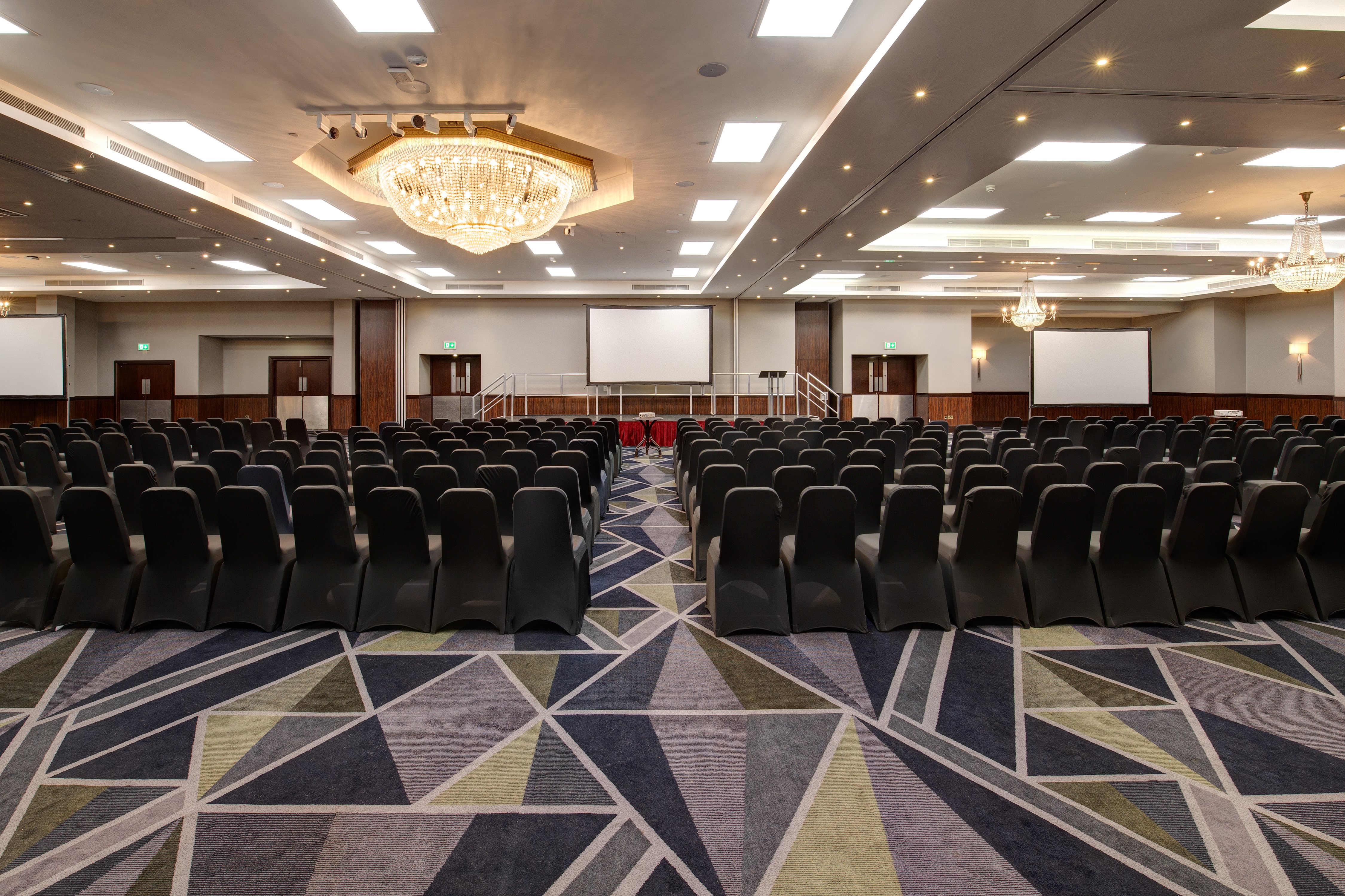 Conference room setup with black chairs and stage for presentations at Royal National Hotel.