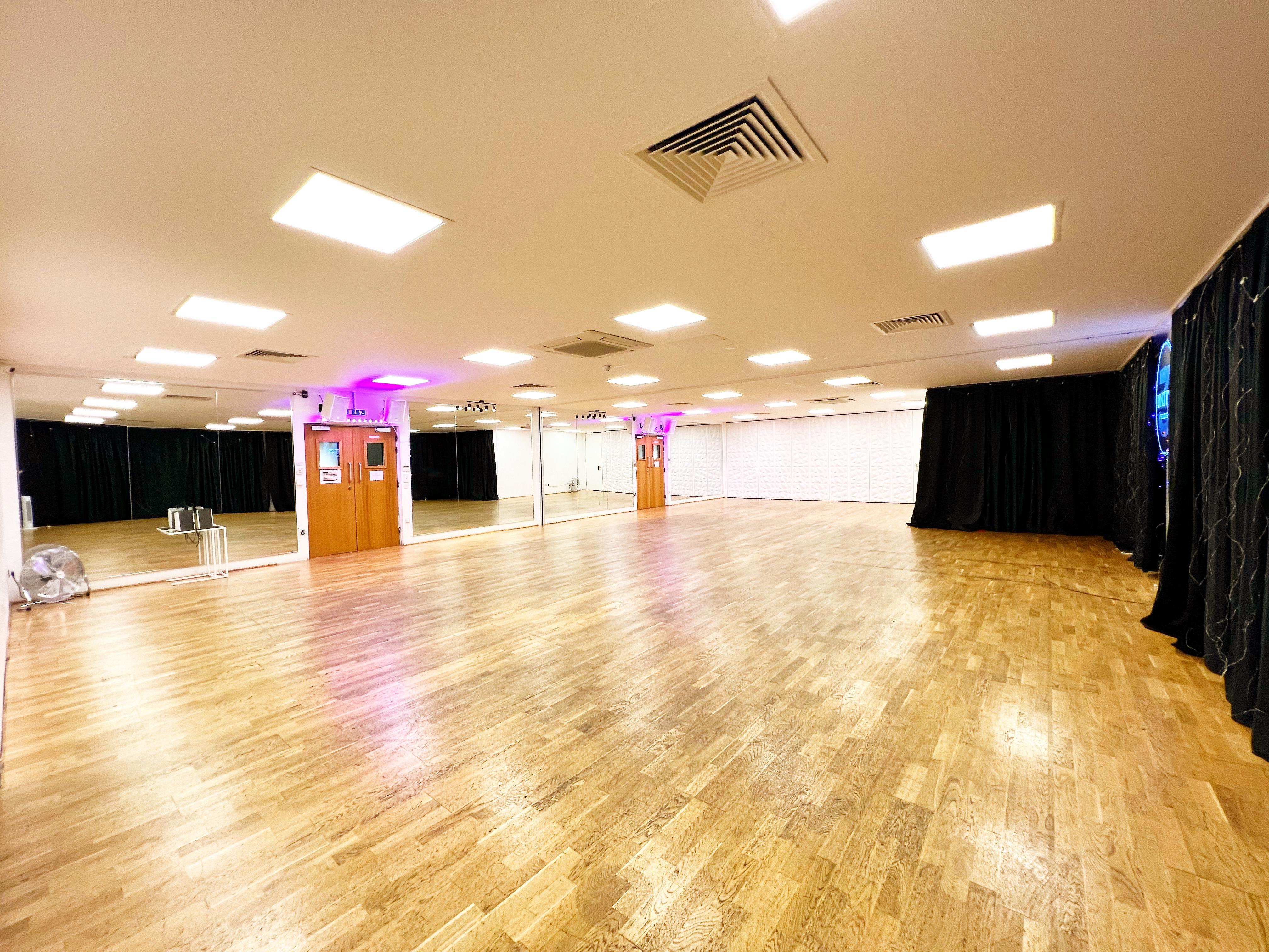Versatile event space with polished wooden floors and mirrors for workshops and dance classes.