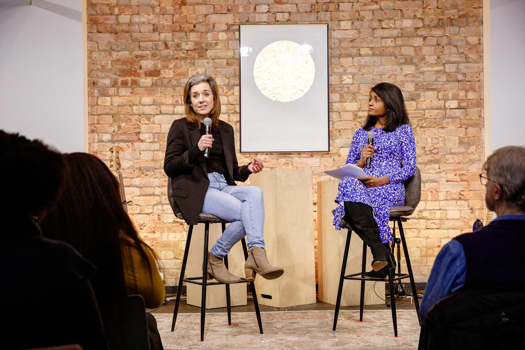 Hybrid event panel discussion with speakers in stylish brick venue, live streaming music.