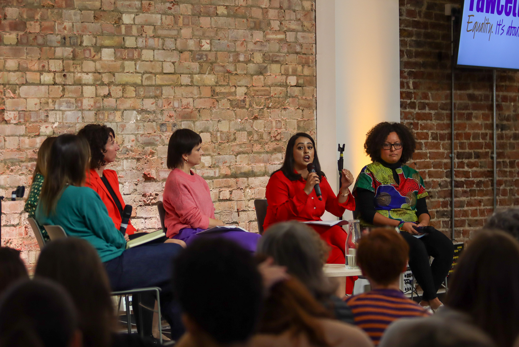Diverse panel discussion at King's House workshop with engaged audience and brick wall backdrop.