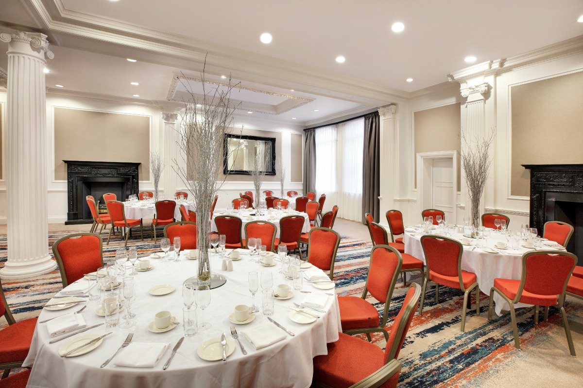 Wedgewood Suite at Leonardo Hotel Cardiff, elegant event space with round tables and red chairs.