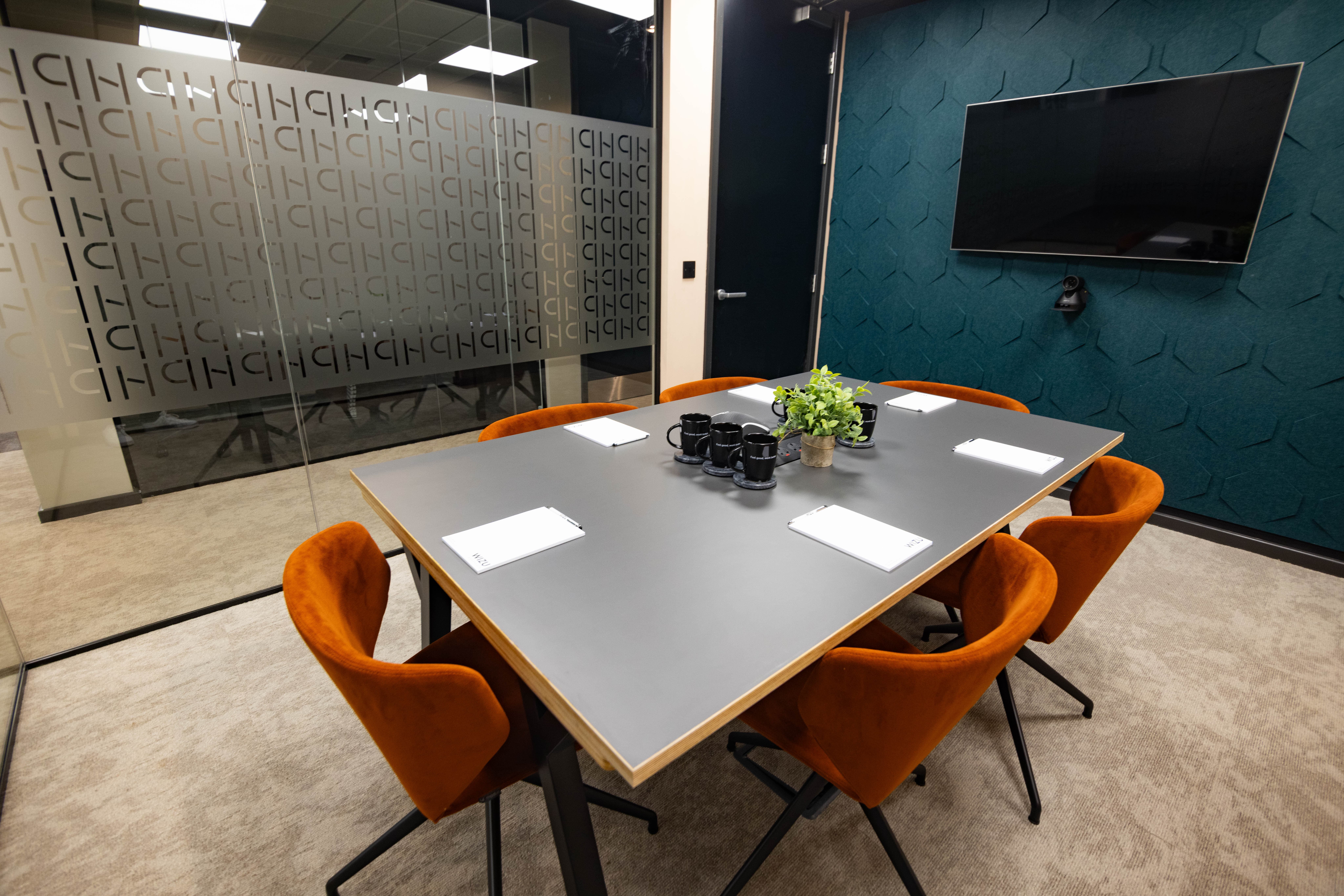 Modern conference room with gray table and orange chairs at Wizu Workspace.