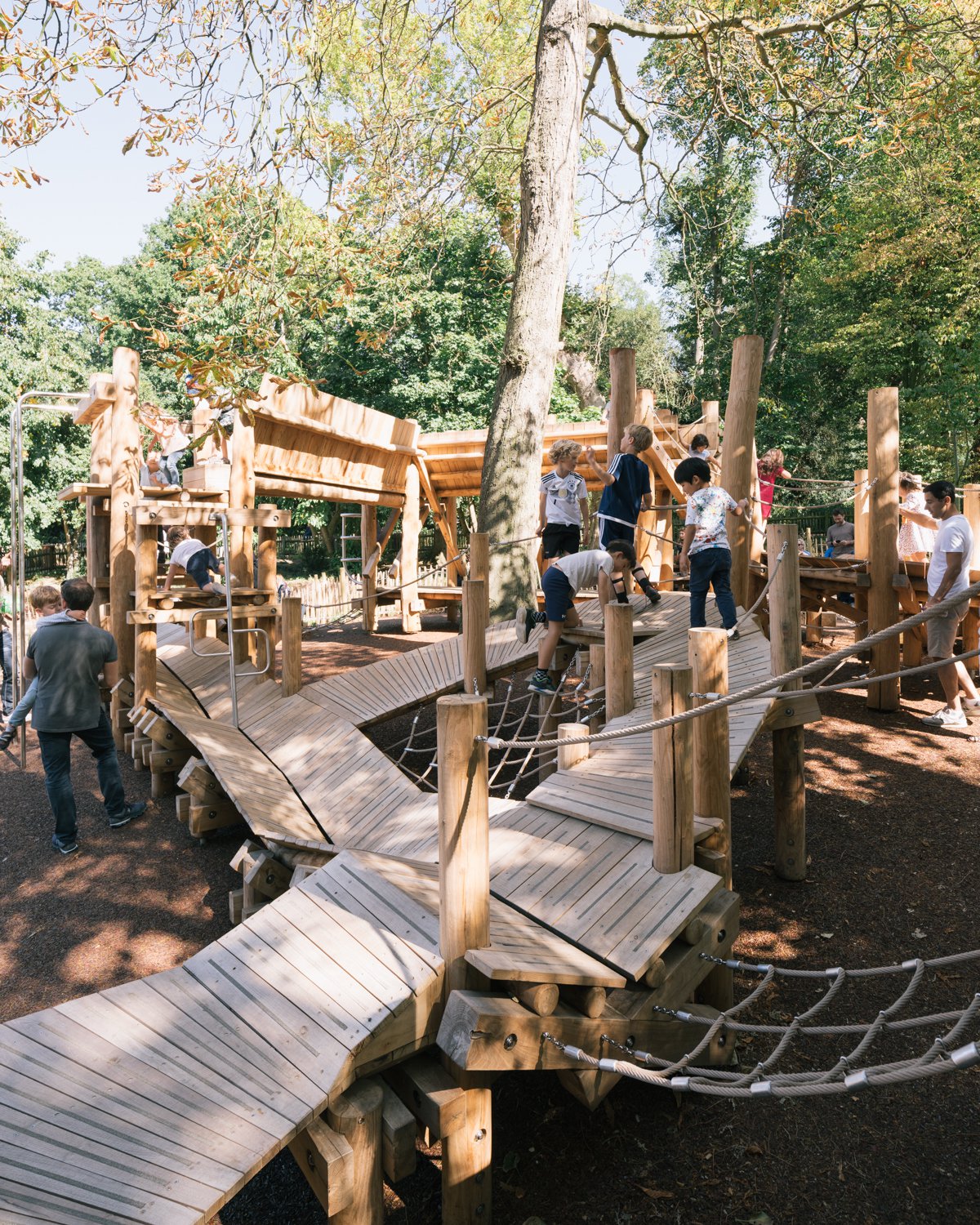 Vibrant playground in Holland Park with wooden climbing structures for family events.
