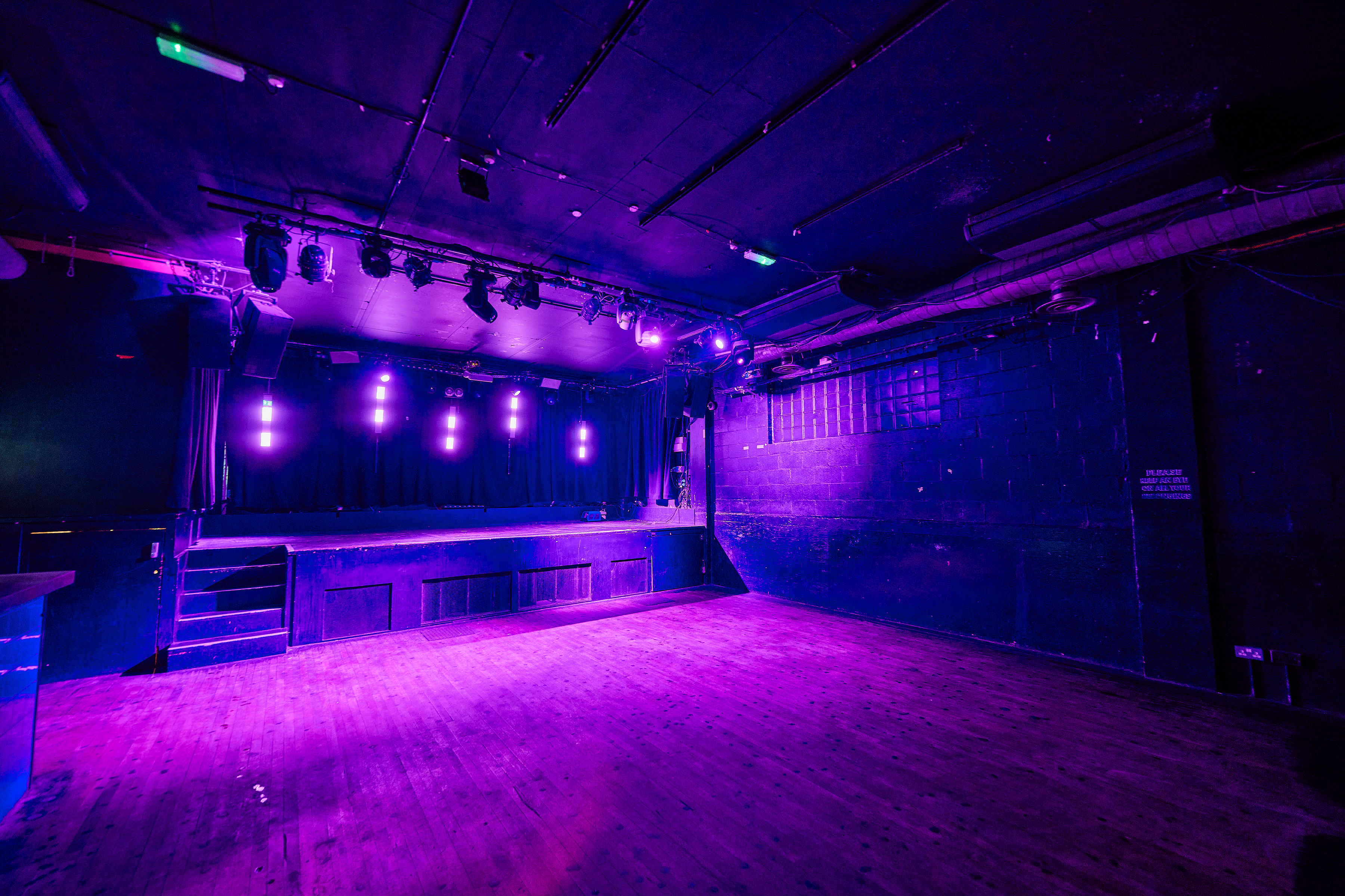 Versatile event space with stage and vibrant purple lighting for live performances.