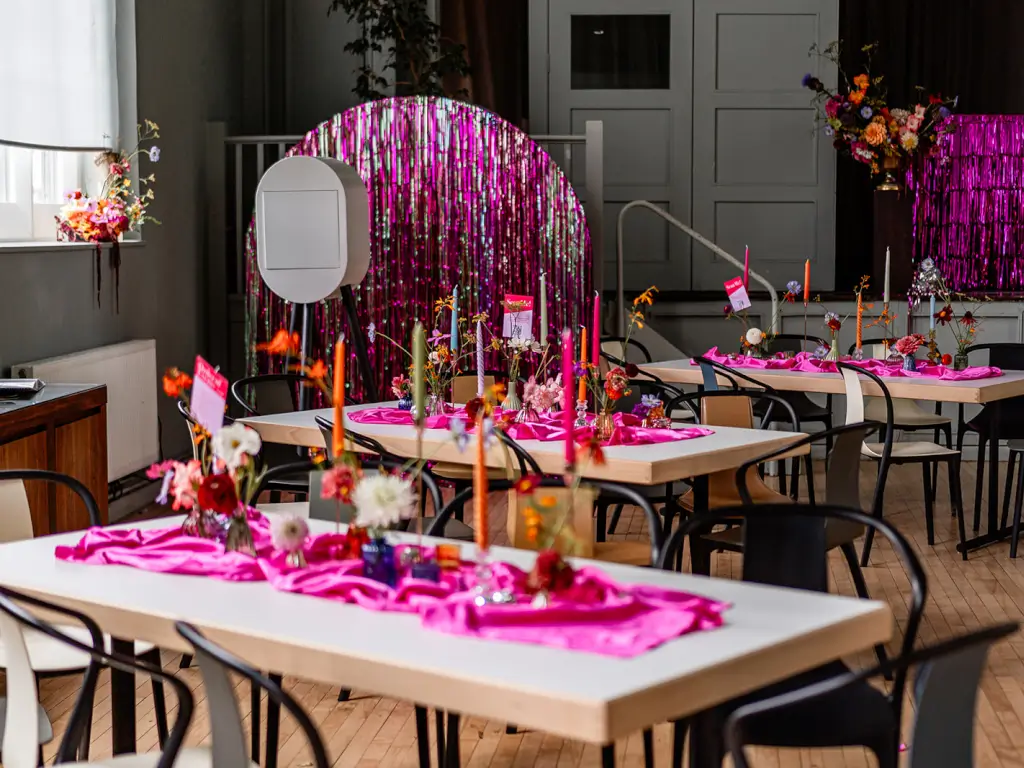 Vibrant event space with pink linens and floral centerpieces for celebrations or workshops.