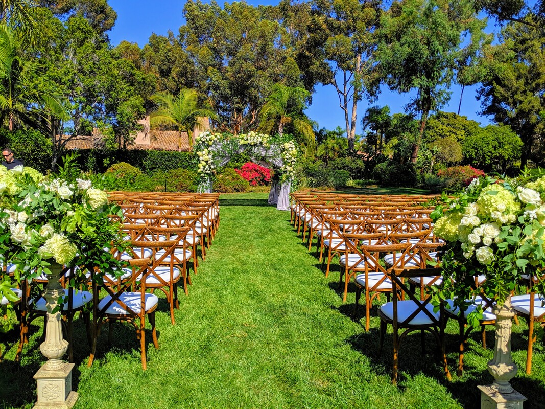 Outdoor wedding ceremony at The Prado with floral arch and wooden chairs.