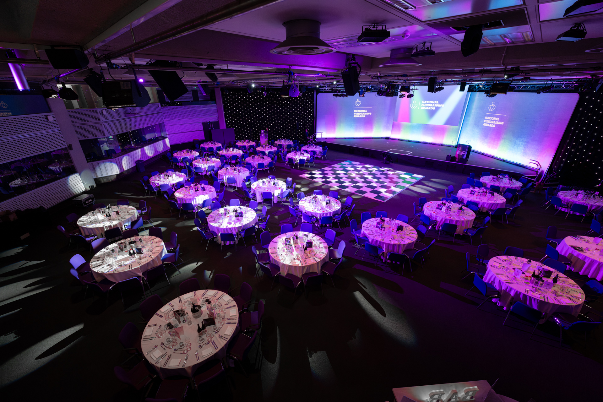 Formal event space at QEII Centre with round tables and stylish stage, ideal for gatherings.
