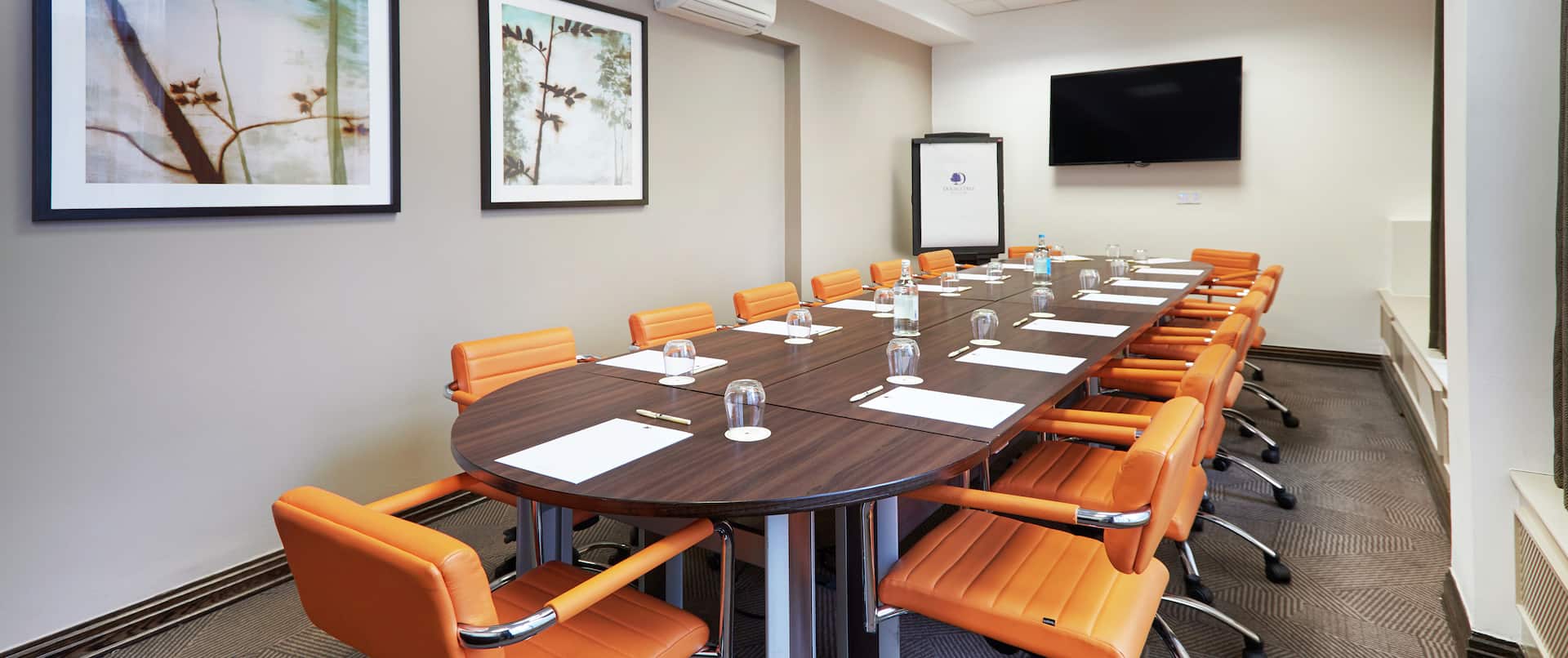 Modern conference room with oval table and vibrant orange chairs at DoubleTree London.