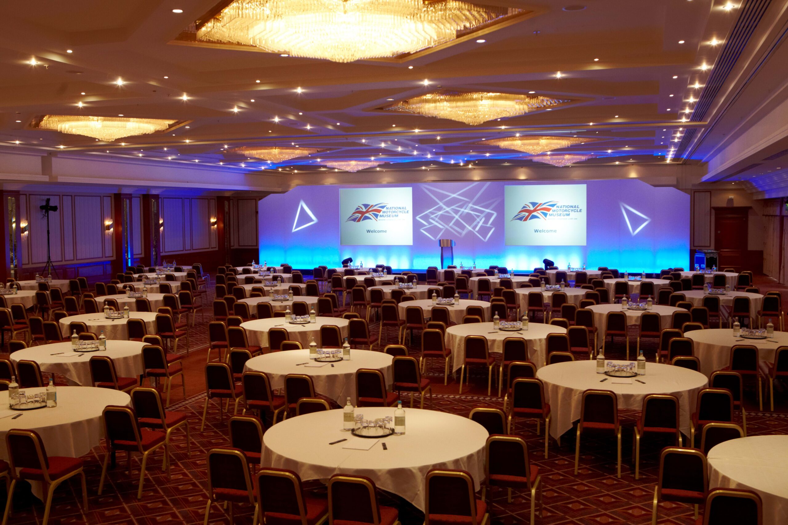 Britannia Suite conference space with round tables and stage for events and networking.