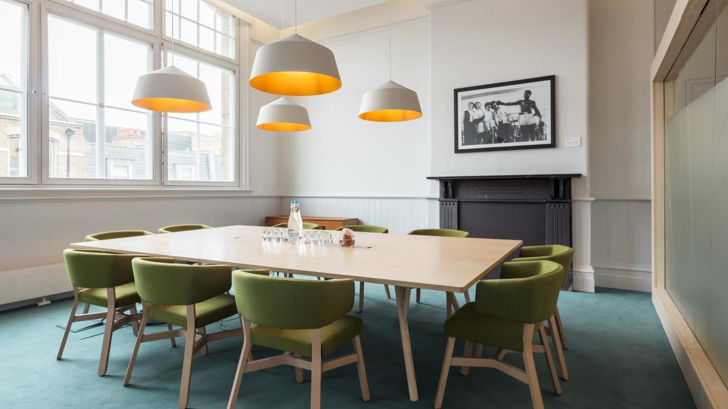 Modern meeting room with wooden table and green chairs at St Pancras Meetings & Events.