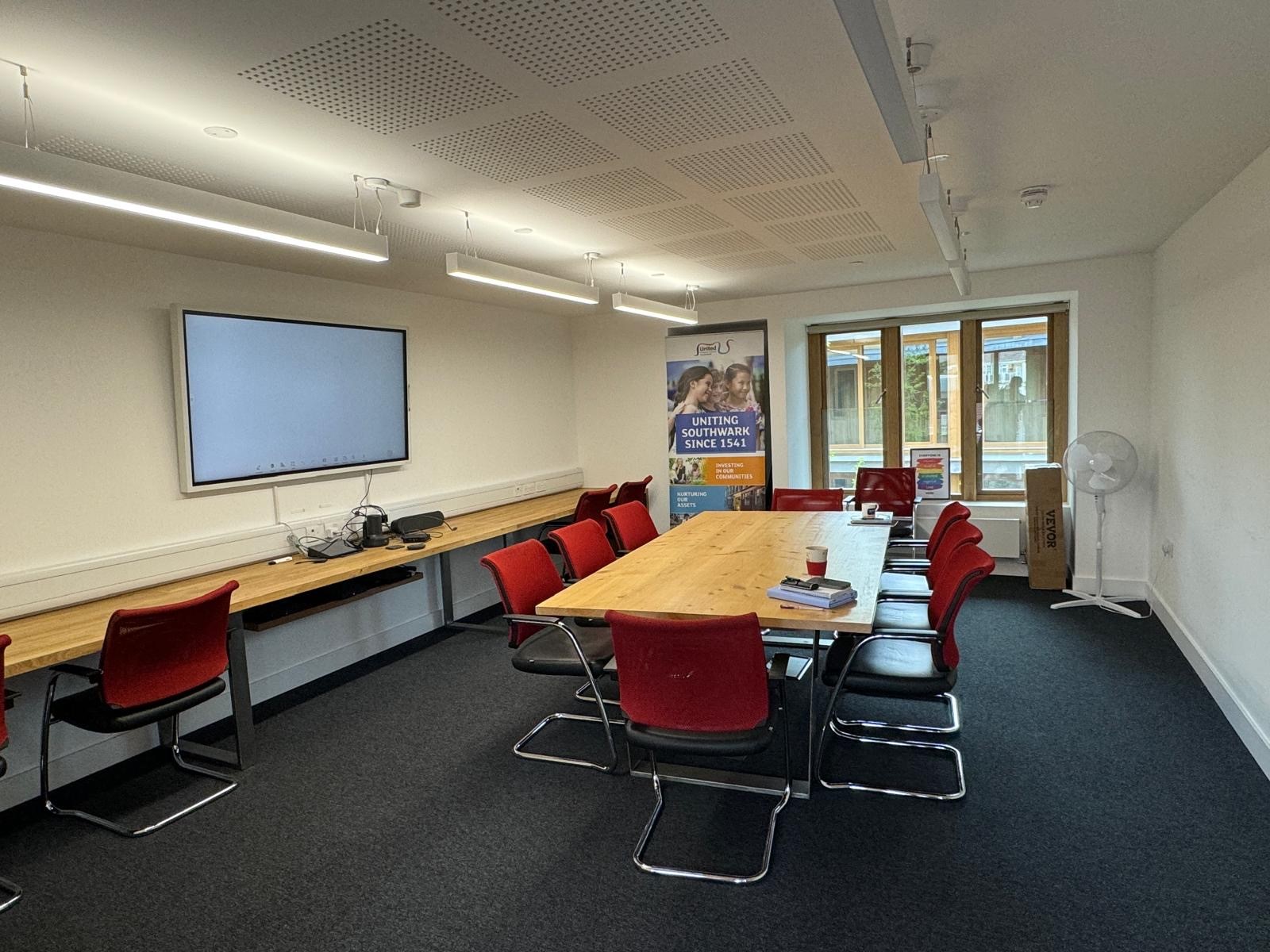 Modern meeting room with wooden table and red chairs, perfect for workshops and team meetings.