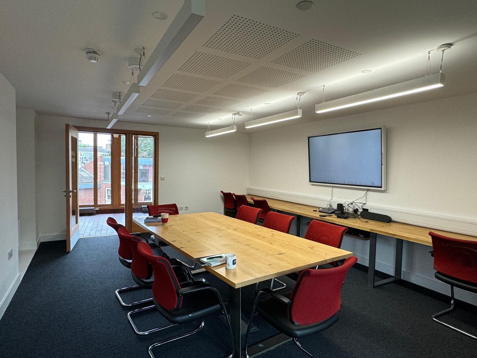 Modern meeting room with wooden table and red chairs, ideal for collaboration and presentations.