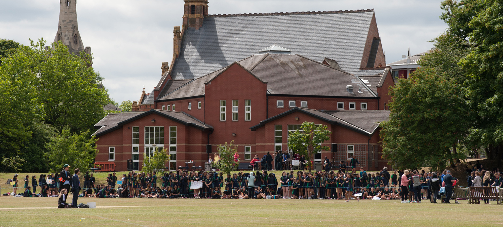 Outdoor event at King Edward VI Handsworth School, featuring a large crowd and vibrant greenery.