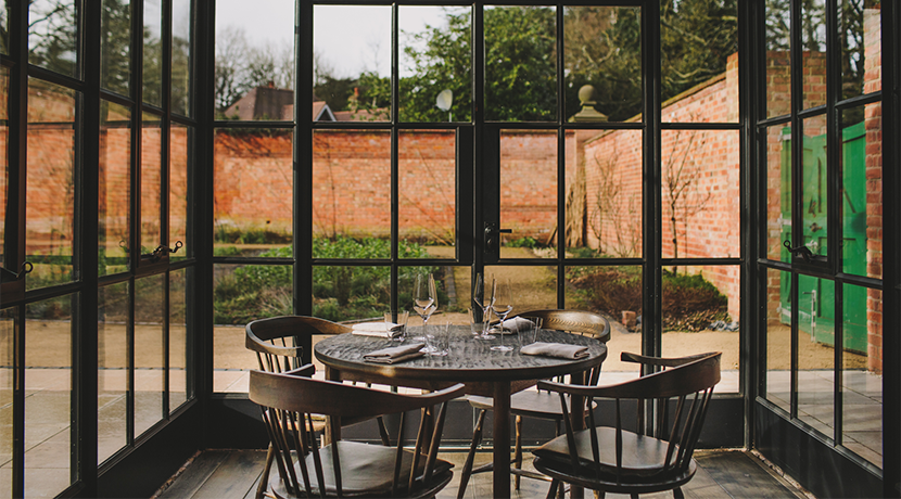 Intimate dining space at Hampton Manor with large windows and rustic brick walls.