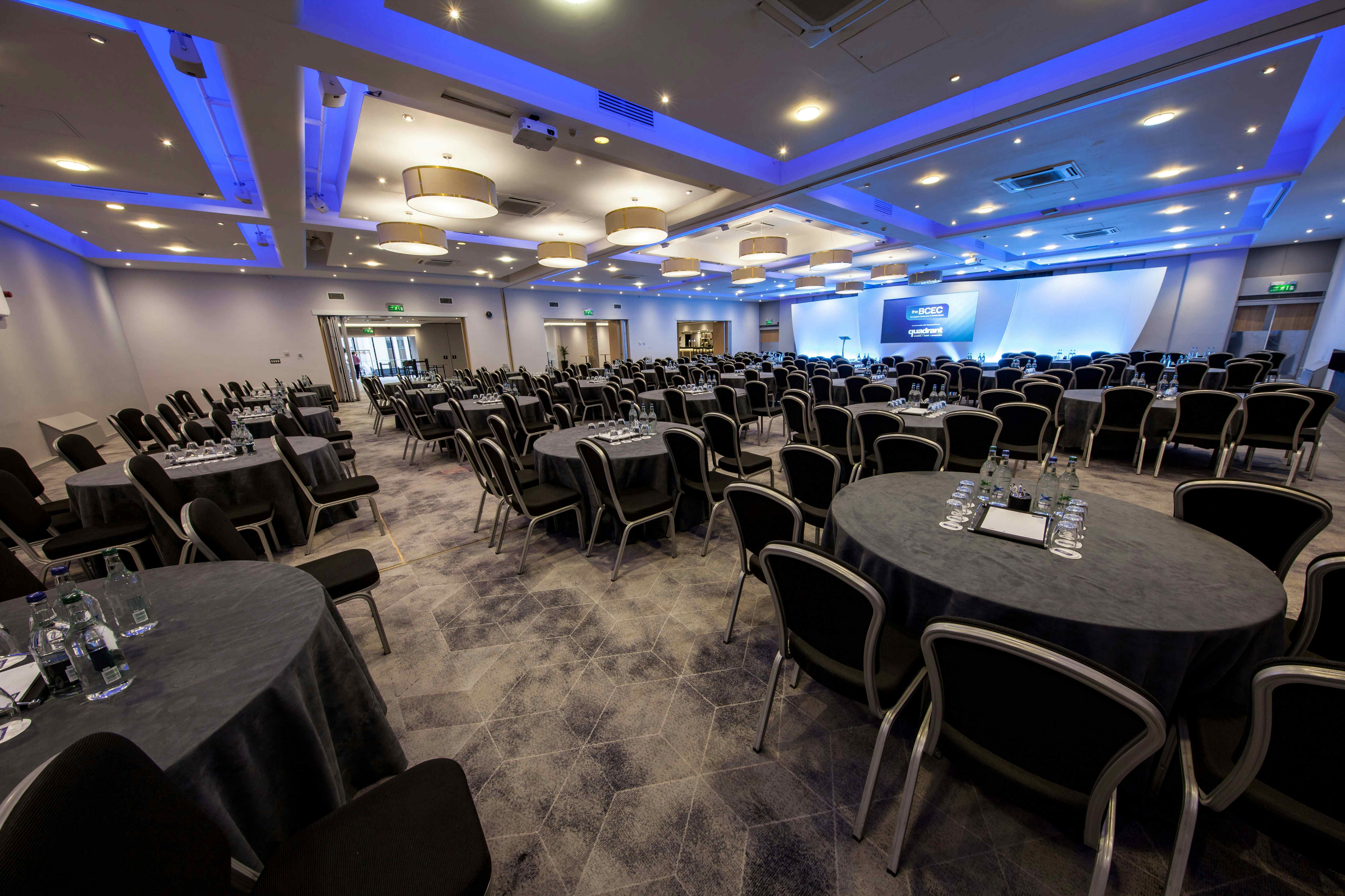 Spacious conference venue with round tables and blue lighting for corporate events.