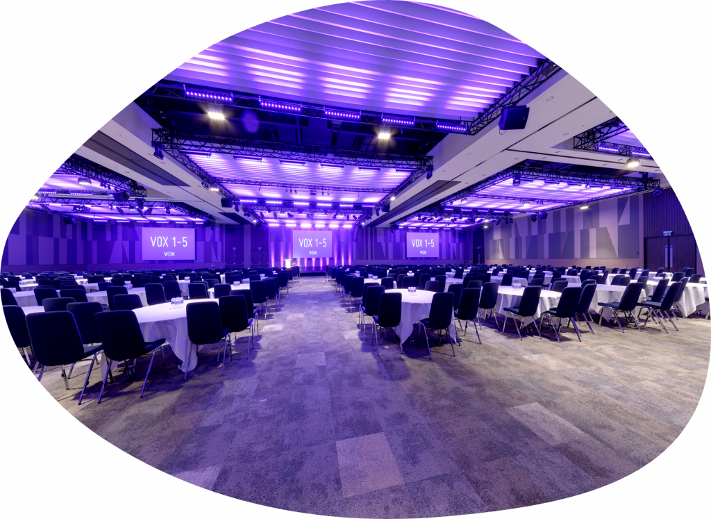 Spacious Vanessa Lounge conference venue with round tables and vibrant purple lighting.
