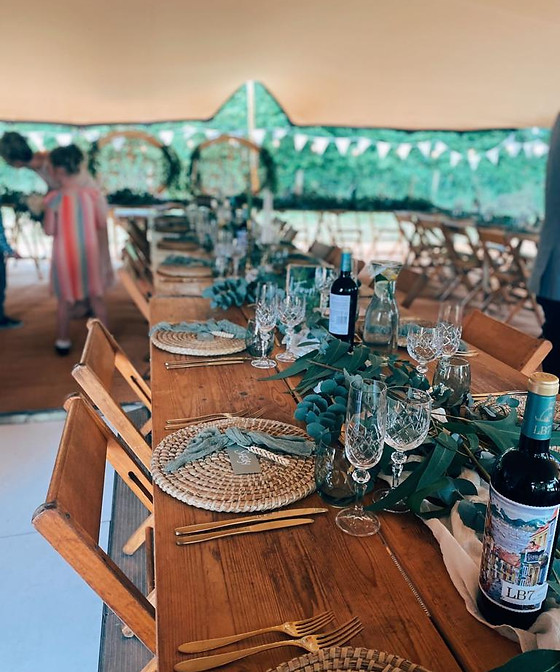 Outdoor dining setup with wooden tables, glassware, and greenery for elegant events.
