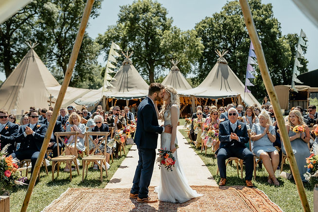 Outdoor wedding ceremony at Belcote Farm with rustic arch and vibrant florals.