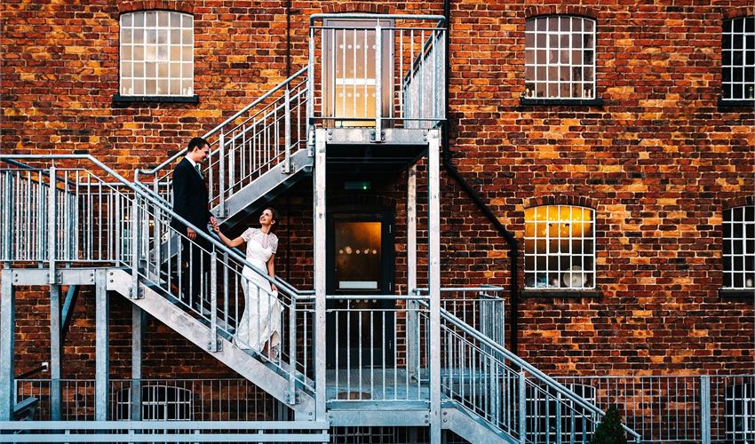 Couple on metal staircase at rustic brick venue for elegant industrial wedding.