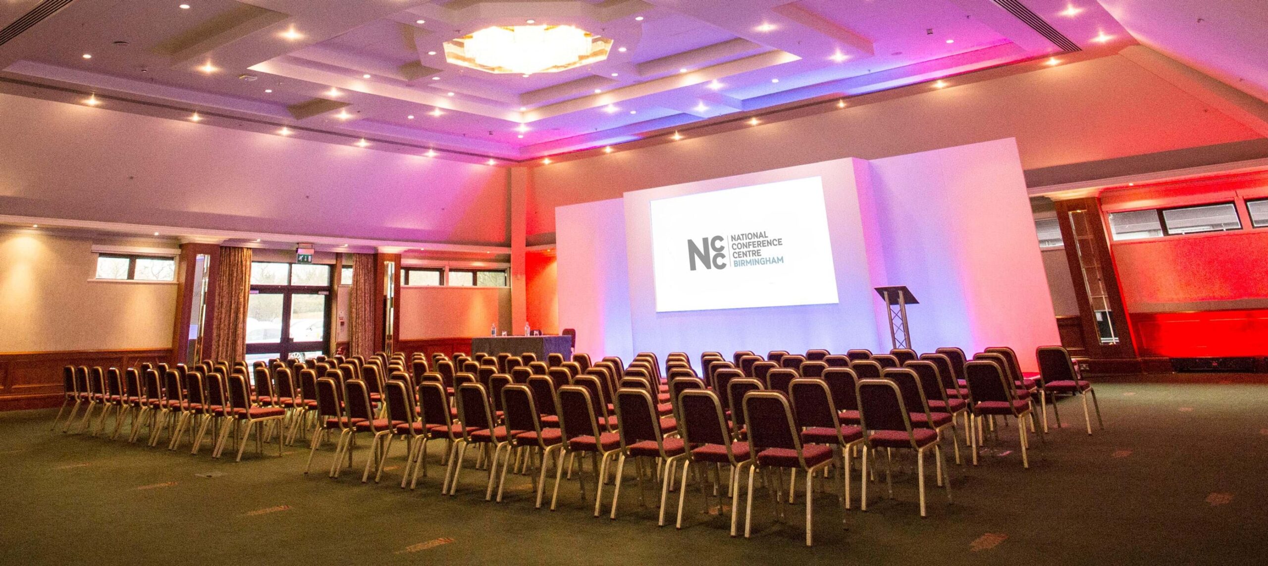 Conference room setup with chairs and screen, ideal for presentations and events.