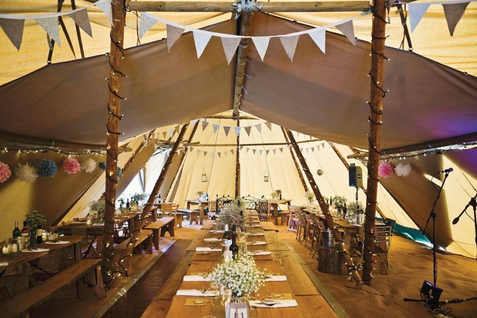 Rustic wedding tent with wooden tables, floral centerpieces, and festive bunting decor.