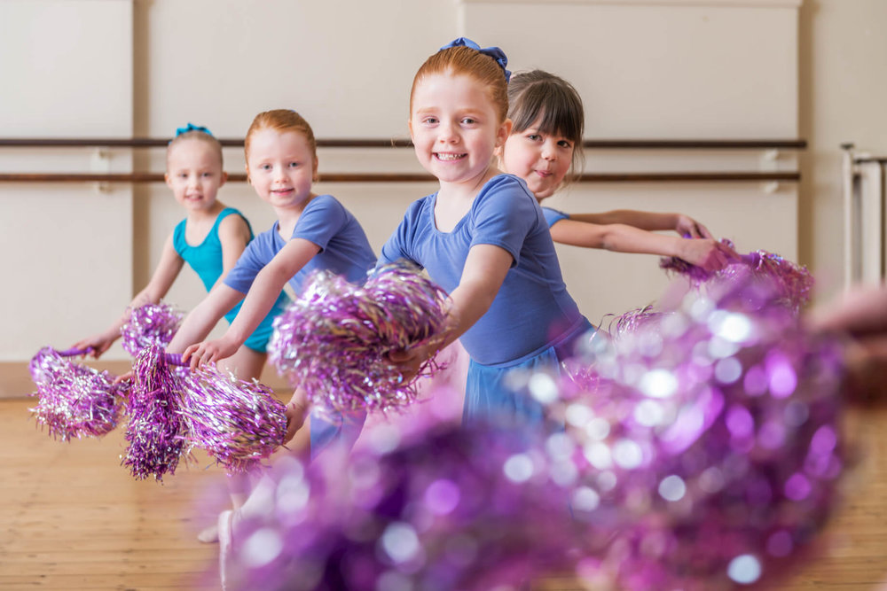 Young dancers in colorful outfits practicing with pom-poms at a children's event.