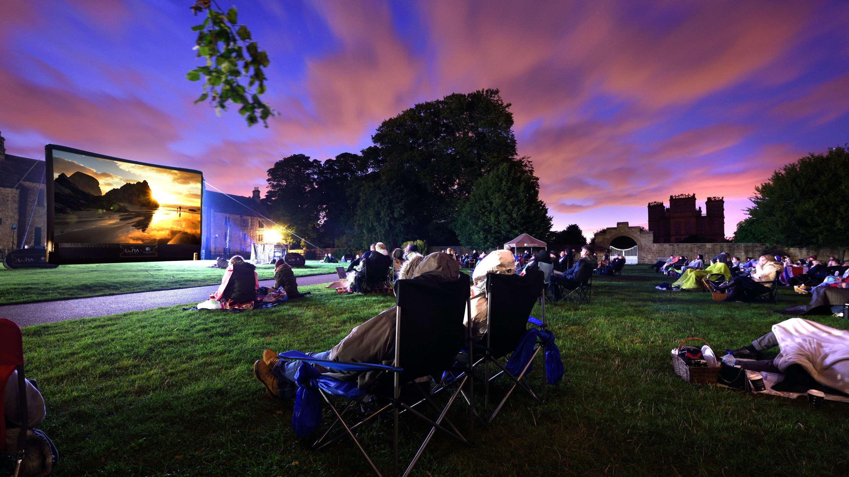 Outdoor movie screening with large screen and sunset backdrop for weddings and events.