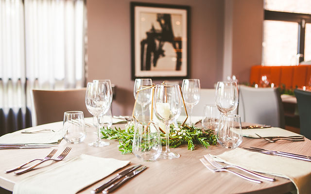 Elegant dining table setup with glassware and greenery for corporate events.