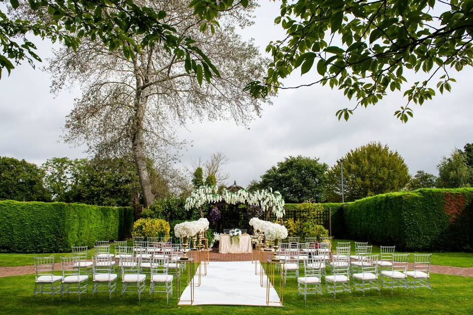 Outdoor wedding venue at Lea Marston Hotel with elegant chairs and floral arch.