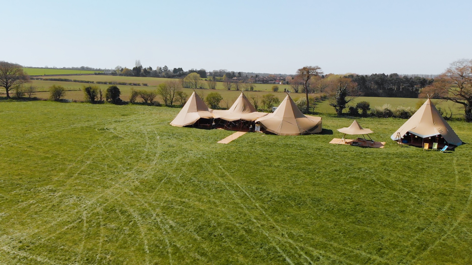 Spacious outdoor event venue with tents in a scenic green field, ideal for weddings and festivals.