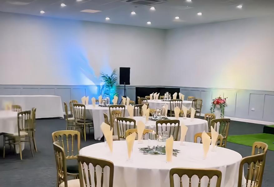 Elegant banquet setup with round tables and yellow napkins at Hall Green Stadium.