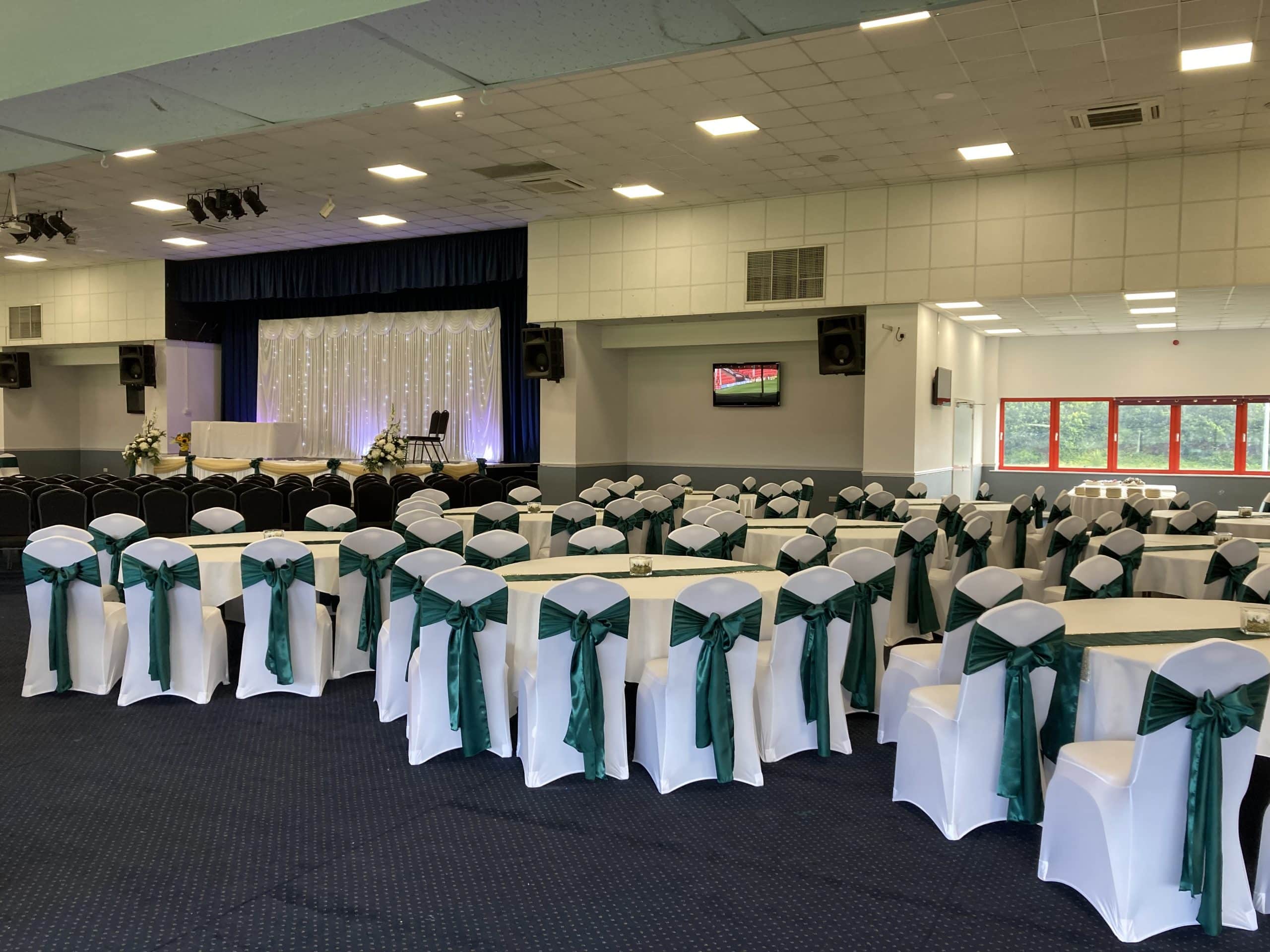 Elegant event space with white tables and green sashes for conferences or weddings.