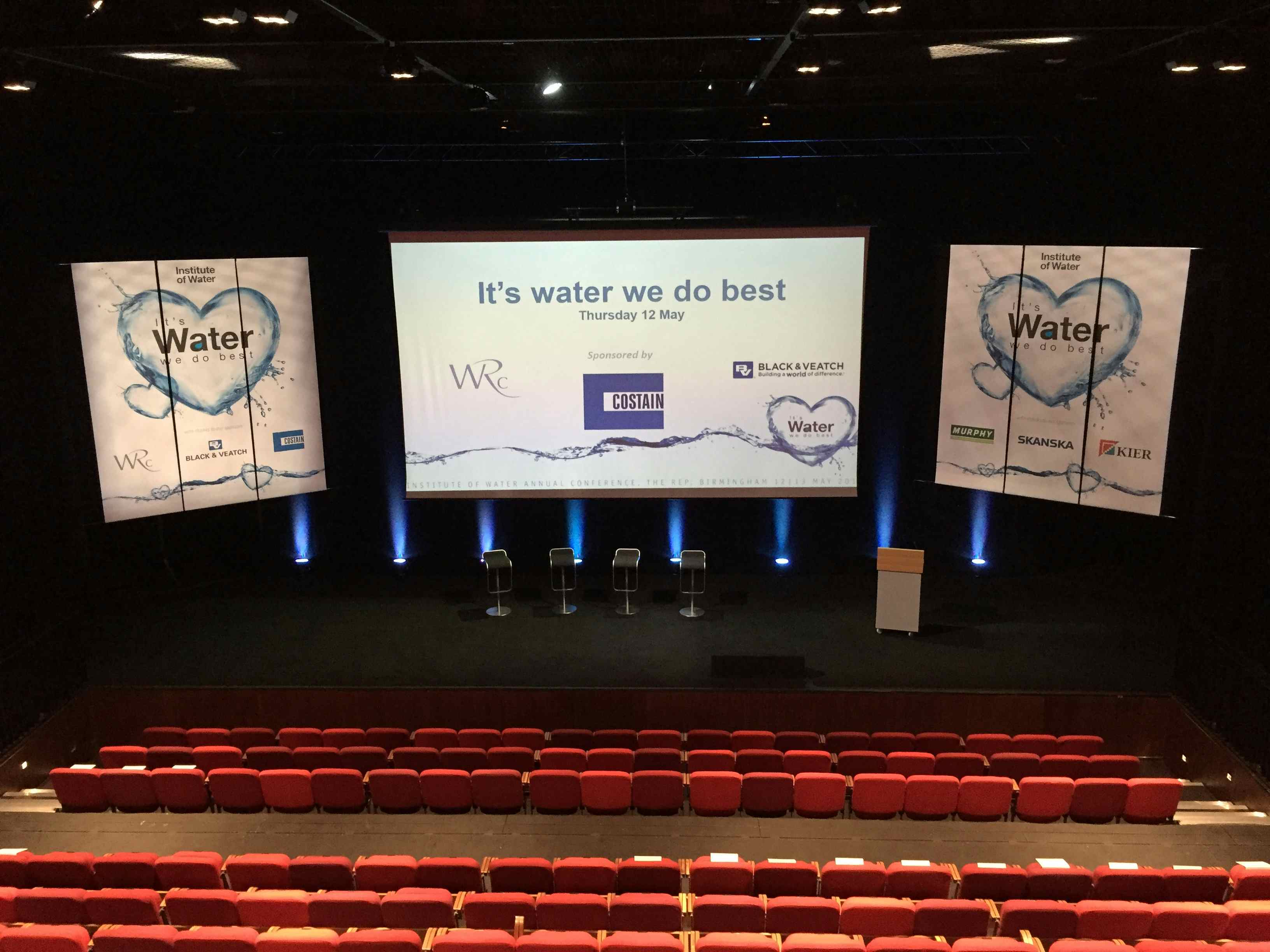 Conference stage at Birmingham Repertory Theatre with water-themed backdrop and seating.