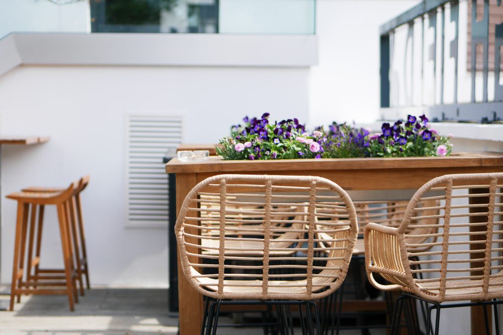 Stylish outdoor event space with wooden table, elegant seating, and vibrant flowers.