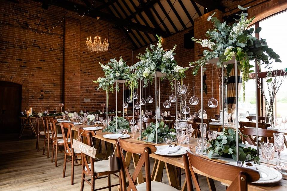 Elegant event space in The Barn with long tables, greenery, and chandelier for weddings.