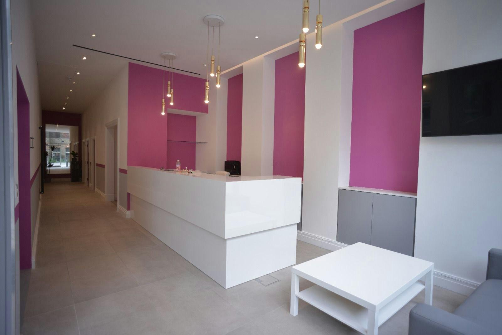 Modern reception area with sleek white desk and pink walls, ideal for events and meetings.
