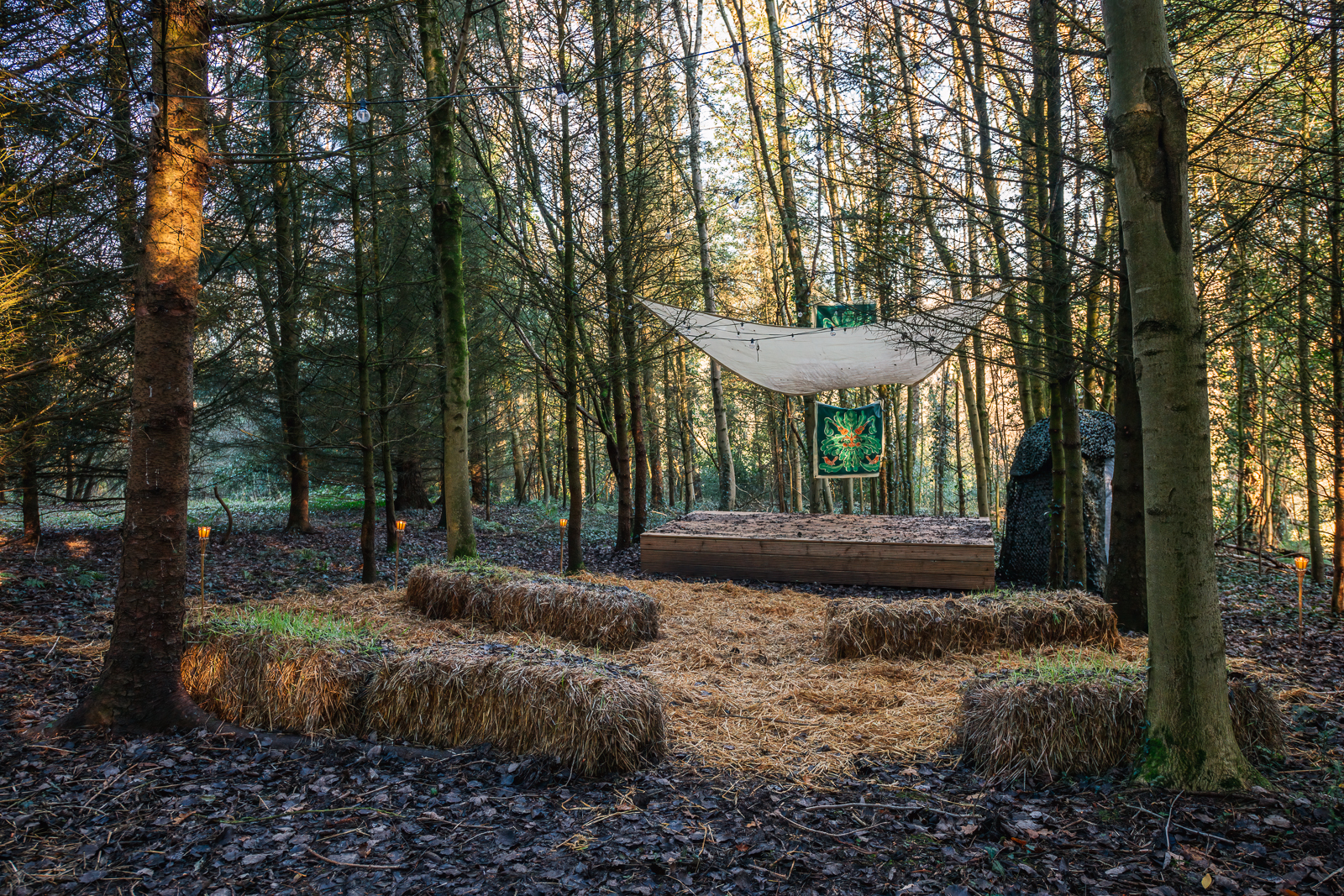 Woodland stage with hay bale seating for outdoor creative events in a forest setting.