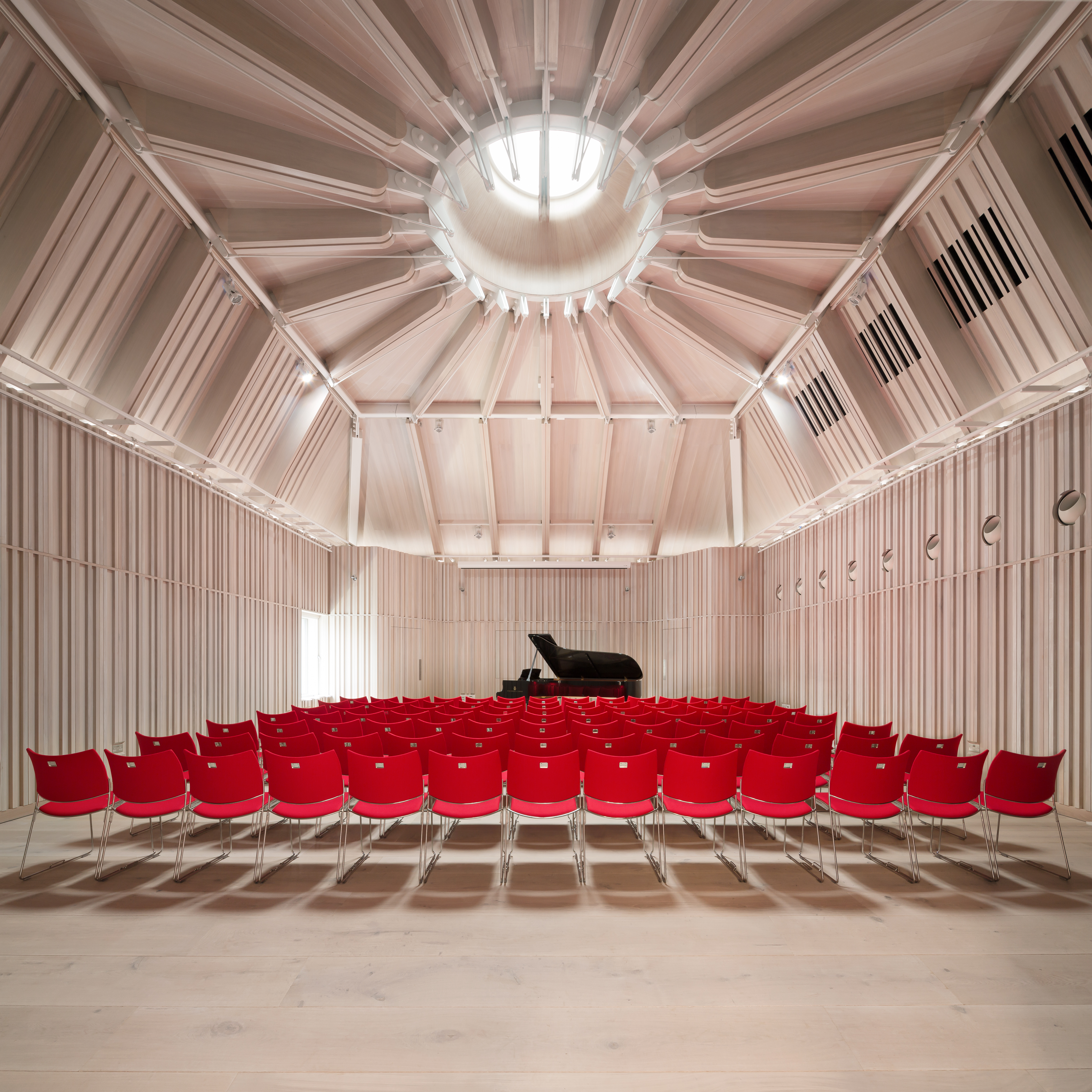 Angela Burgess Recital Hall with grand piano, vibrant red chairs for concerts and lectures.