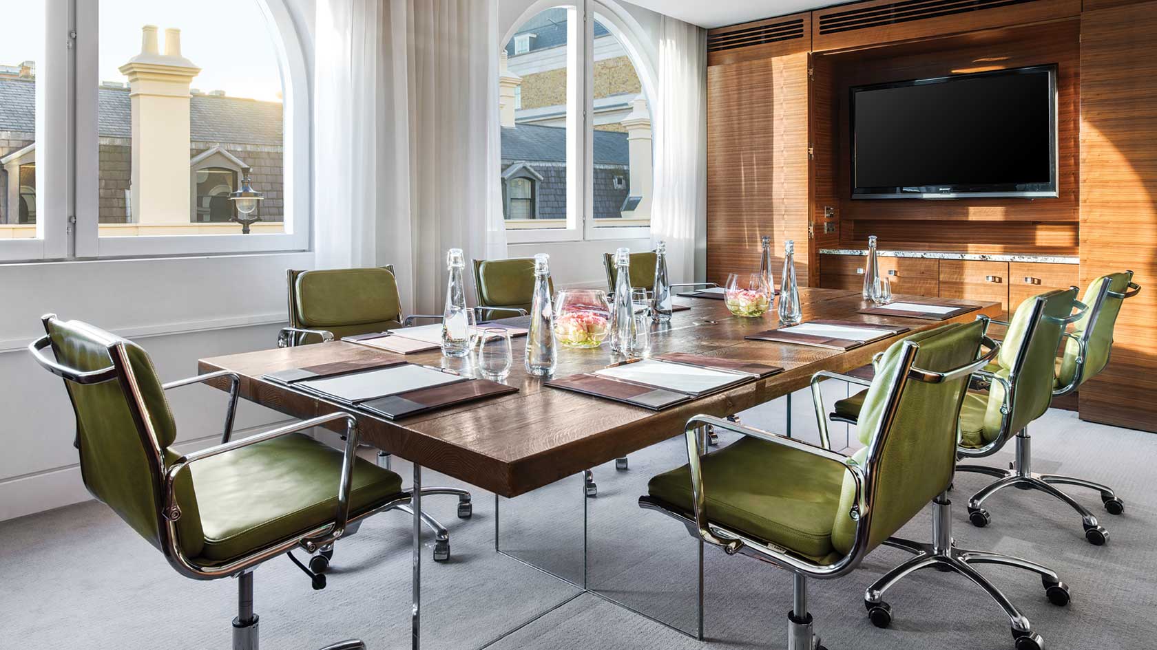 Modern meeting room at The Langham, London with natural light and green chairs.