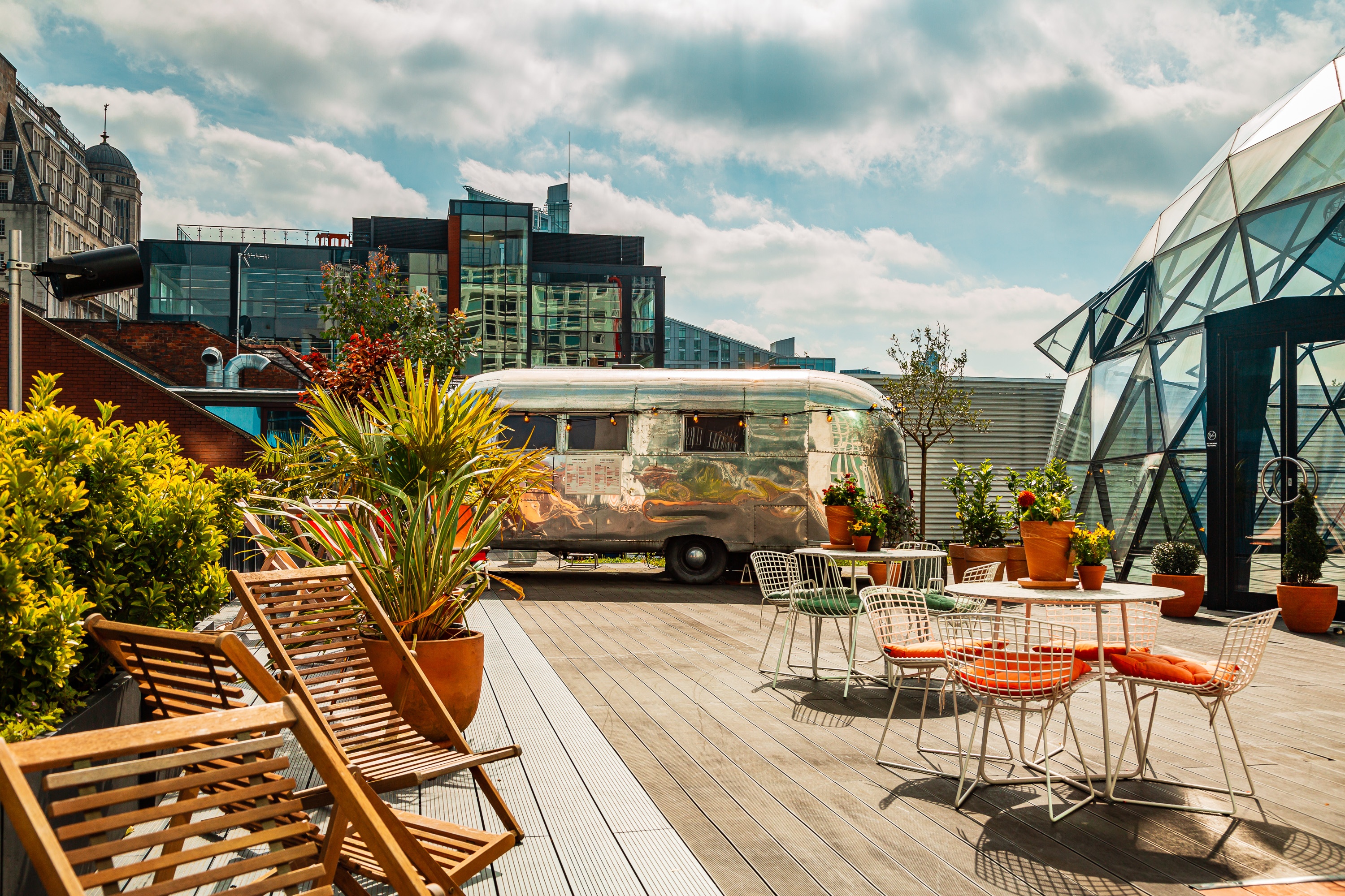 Vibrant rooftop event space with stylish seating and vintage Airstream trailer for gatherings.