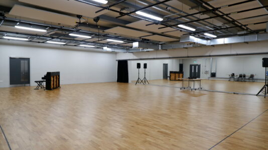 Spacious rehearsal suite with wooden flooring, ideal for workshops and corporate events.
