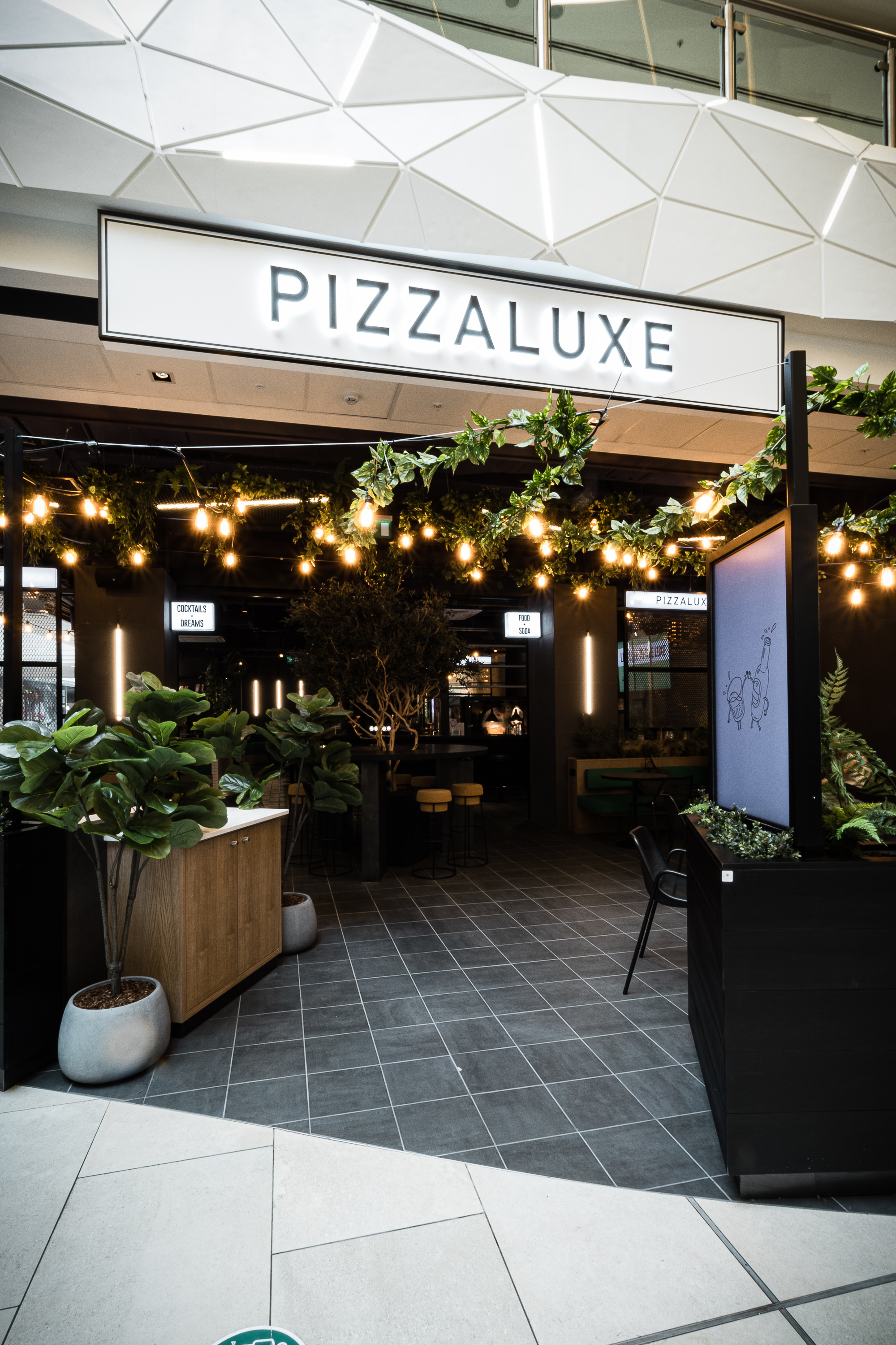 Exclusive Hire event space in PizzaLuxe Manchester with lush greenery and warm lighting.