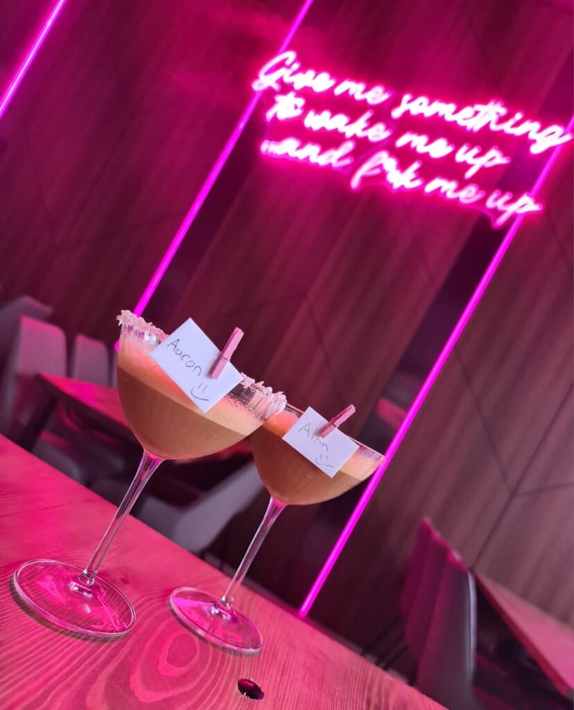 Elegant cocktails with name tags in a vibrant neon-lit cocktail bar setting.