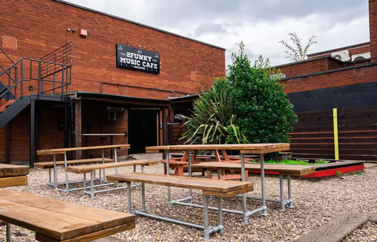 Outdoor event space at 2Funky Lounge with rustic tables for music gatherings.