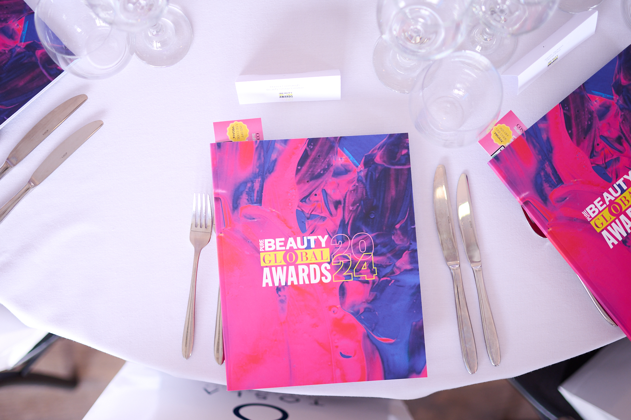 "Elegant table setting for Beauty Global Awards 2024 in OXO2, featuring vibrant program booklets."