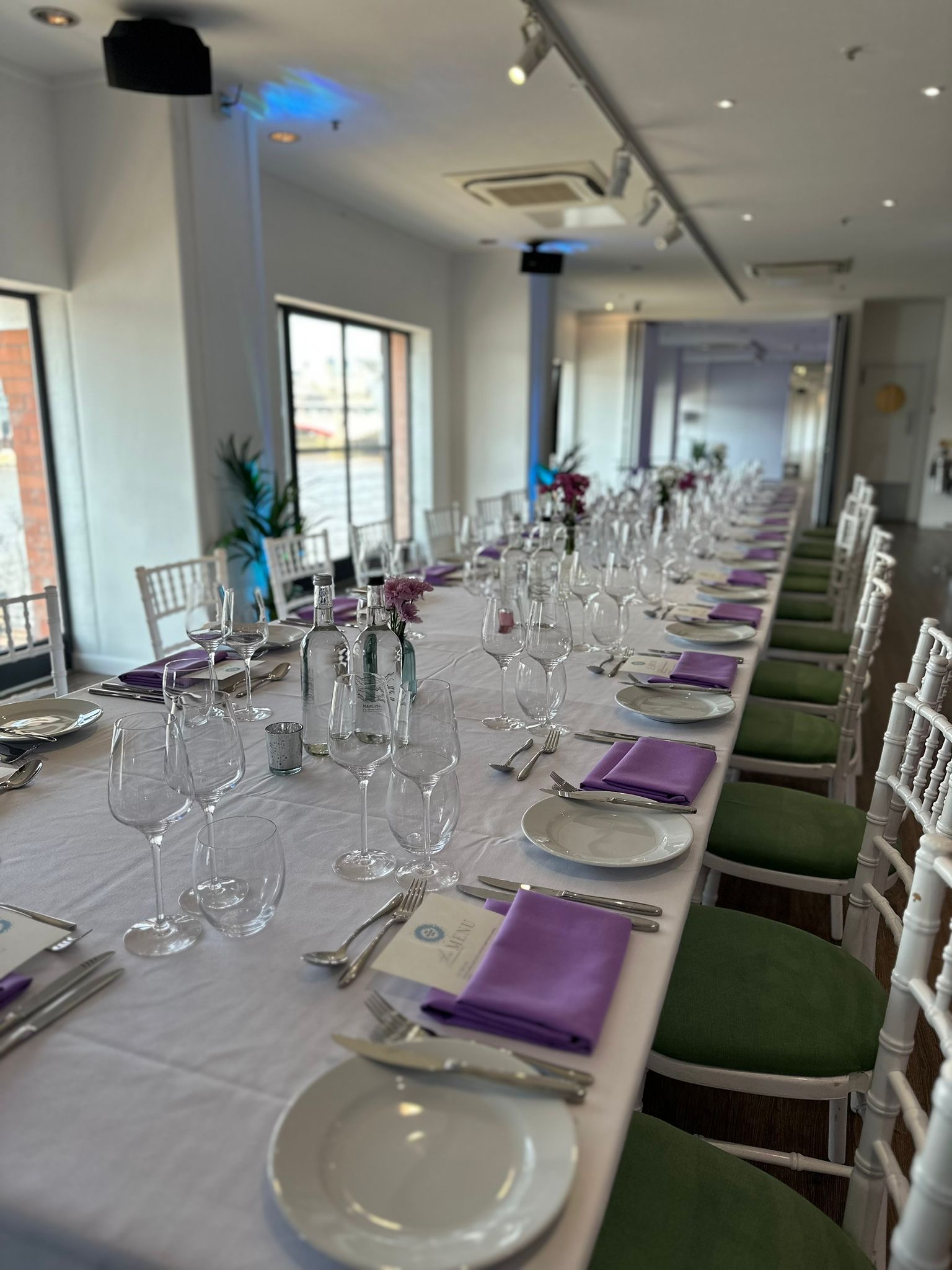 Elegant long table setup with white linens and purple napkins for corporate events.