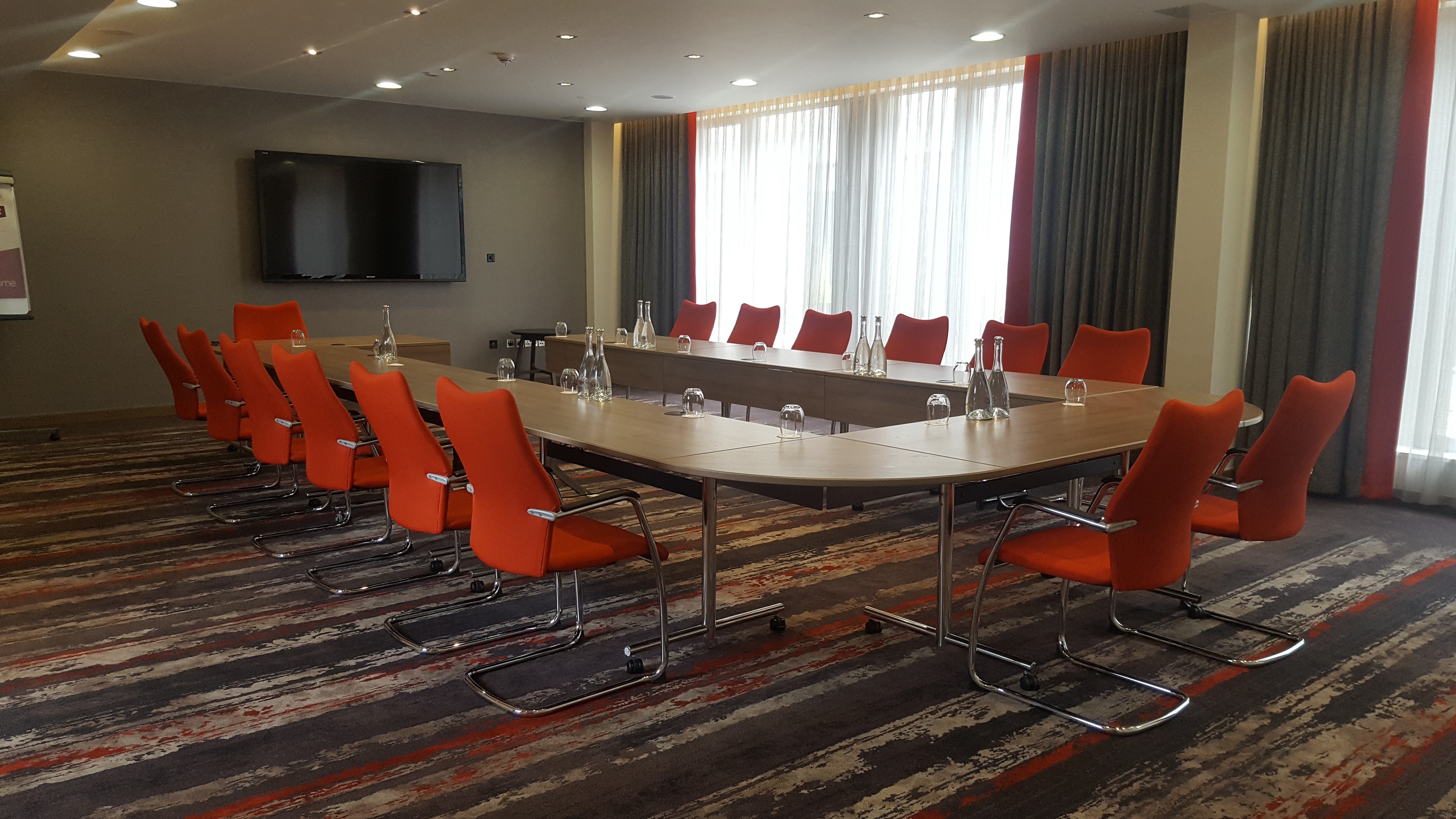 Modern meeting room in Clayton Hotel Chiswick with oval table and orange chairs.
